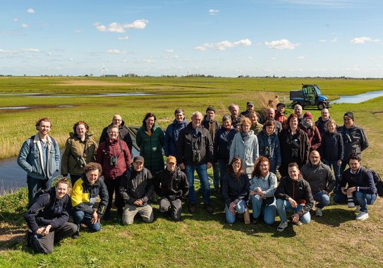 Group photo of around 30 people standing in a sunny meadow.
